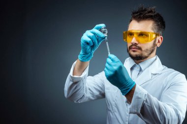 Male scientist, laboratory assistant in a white coat and glasses holds a bottle with a vaccine in his hands, medical tests, laboratory, experiments. Immunization chemical analysis.