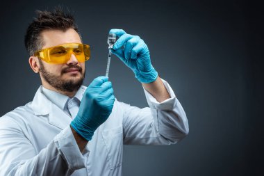 Male scientist, laboratory assistant in a white coat and glasses holds a bottle with a vaccine in his hands, medical tests, laboratory, experiments. Immunization chemical analysis.