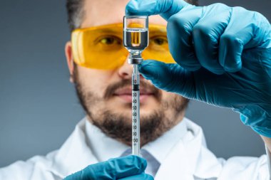 Male scientist, laboratory assistant in a white coat and glasses holds a bottle with a vaccine in his hands, medical tests, laboratory, experiments. Immunization chemical analysis.