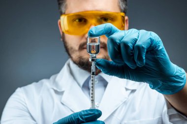 Male scientist, laboratory assistant in a white coat and glasses holds a bottle with a vaccine in his hands, medical tests, laboratory, experiments. Immunization chemical analysis.