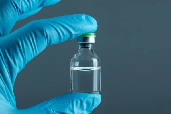 Рука в синій рукавичці тримає пляшку з вакциною крупним планом на сірому фоні, медична концепція вакцинації підшкірної ін'єкції, доза. Лікування хвороби імунізація . — стокове фото