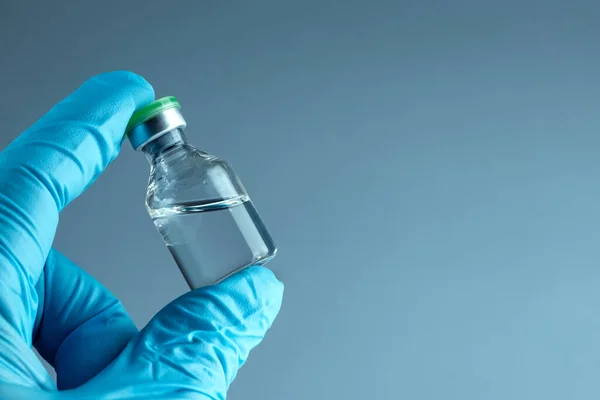 Рука в синій рукавичці тримає пляшку з вакциною крупним планом на сірому фоні, медична концепція вакцинації підшкірної ін'єкції, доза. Лікування хвороби імунізація . — стокове фото