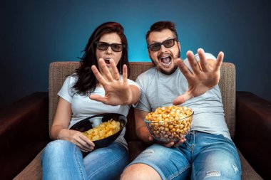 A man and a woman, a family watching a movie or a series in 3D glasses, a blue background. The concept of a cinema, films, emotions, surprise, leisure, streaming platforms.