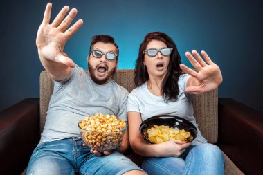 A man and a woman, a family watching a movie or a series in 3D glasses, a blue background. The concept of a cinema, films, emotions, surprise, leisure, streaming platforms.