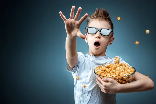 Un niño sosteniendo palomitas de maíz en sus manos viendo una película en gafas 3D, miedo, fondo azul. El concepto de un cine, películas, emociones, sorpresa, ocio. plataformas de streaming . —  Fotos de Stock