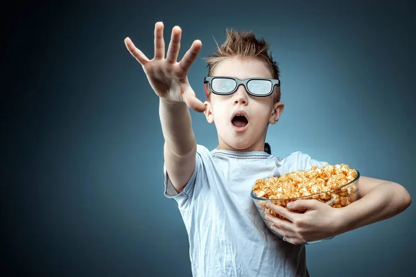 Un garçon tenant du pop-corn dans ses mains regardant un film en lunettes 3D, peur, fond bleu. Le concept de cinéma, films, émotions, surprise, loisirs. plateformes de streaming . — Photo