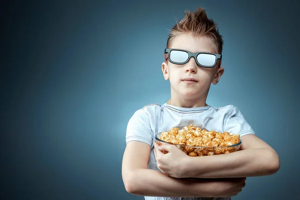 Hält der Junge Popcorn in der Hand und schaut sich einen Film in 3D-Gläsern auf blauem Hintergrund an. das Konzept eines Kinos, Filme, Emotionen, Überraschung, Freizeit. — Stockfoto