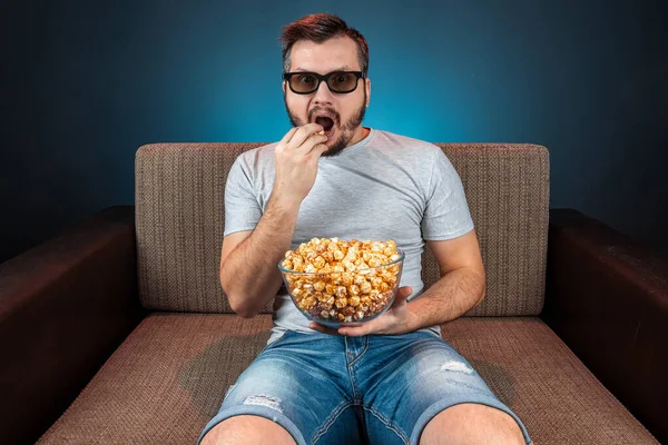 Un homme regarde un film ou une série avec des lunettes 3D, un fond bleu. Le concept de cinéma, films, émotions, surprise, loisirs, plateformes de streaming . — Photo