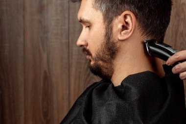 Usta, elektrikli makineyle müşterinin saçını kesiyor, budayıcı, yakın plan. Kuaförde, berberde erkek saç kesimi süreci. Vücut bakımı, yaşam tarzı, metroseksüel..