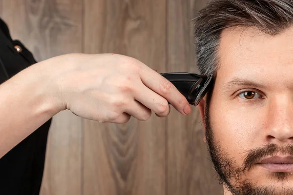 Le maître fait une coupe de cheveux au client avec une machine électrique, tondeuse, gros plan. Le processus de coupes de cheveux masculins chez le coiffeur, salon de coiffure. Soins du corps, mode de vie, métrosexuel . — Photo