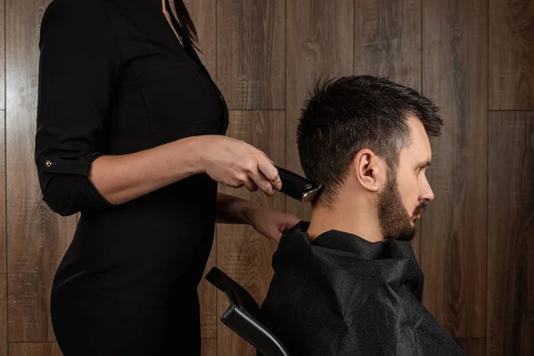 The master makes a haircut to the client with an electric machine, trimmer, close-up. The process of male haircuts at the hairdresser, barbershop. Body care, lifestyle, metrosexual.