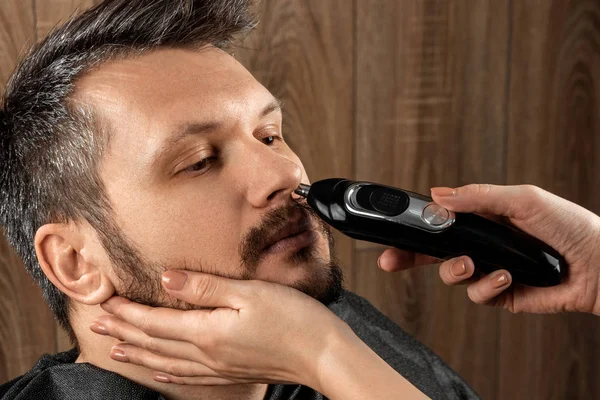 Mestre corta o cabelo do nariz para o cliente com aparador, close-up. O processo no cabeleireiro, barbearia. Cuidados com o corpo, estilo de vida, metrosexual . — Fotografia de Stock