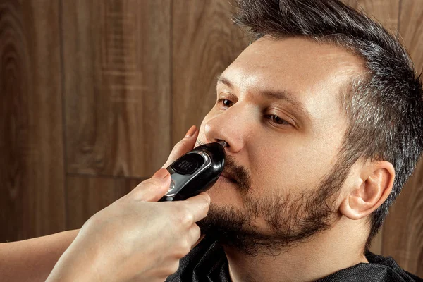 Mestre corta o cabelo do nariz para o cliente com aparador, close-up. O processo no cabeleireiro, barbearia. Cuidados com o corpo, estilo de vida, metrosexual . — Fotografia de Stock