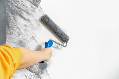 Kadın eli yakın plan bir duvarı griye boyar. Onarım, değişim, tasarım, iç tavan arası konsepti