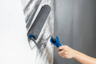 Kadın eli yakın plan bir duvarı griye boyar. Onarım, değişim, tasarım, iç tavan arası konsepti