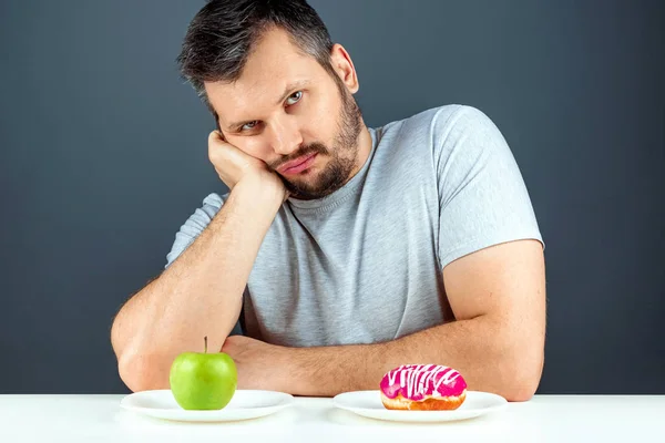 大人の男はドーナツと緑のリンゴの間で選択します。概念誘惑への抵抗、ファーストフード、健康的な食べ物、食事、ボディケア. — ストック写真