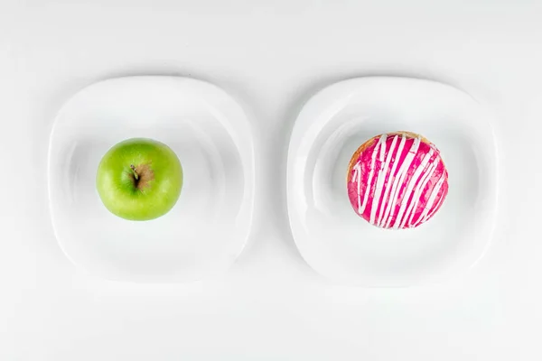 Ένα ντόνατ και ένα πράσινο μήλο βρίσκονται στην πάνω όψη πιάτα, η σωστή επιλογή. Αντίσταση στον πειρασμό, fast food, υγιεινά τρόφιμα, διατροφή. — Φωτογραφία Αρχείου