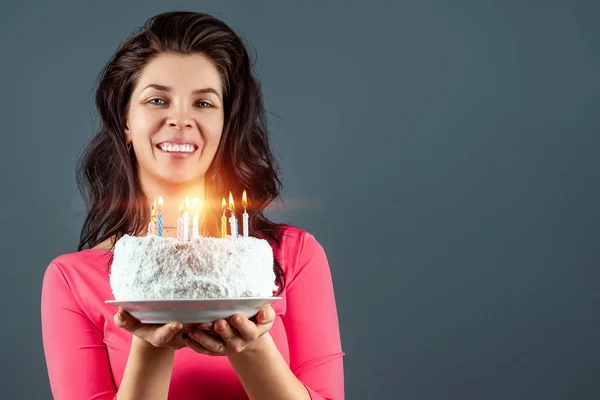 Piękna młoda dziewczyna w różowej sukience trzyma tort w dłoniach z płonącymi świecami, zbliżenie. Wszystkiego najlepszego z okazji urodzin. Przestrzeń kopiowania. — Zdjęcie stockowe