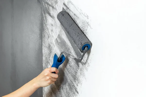 A mão feminina closeup pinta uma parede no cinza. O conceito de reparação, mudança, design, loft interior — Fotografia de Stock