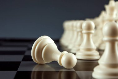 Yakın plan beyaz piyon satranç tahtasında, satrançta ve oyunda yatıyor. Yüzleşme, yıkım, kayıp, ölüm kavramı