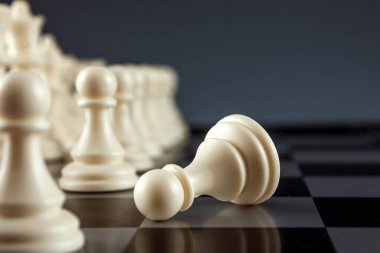 Yakın plan beyaz piyon satranç tahtasında, satrançta ve oyunda yatıyor. Yüzleşme, yıkım, kayıp, ölüm kavramı