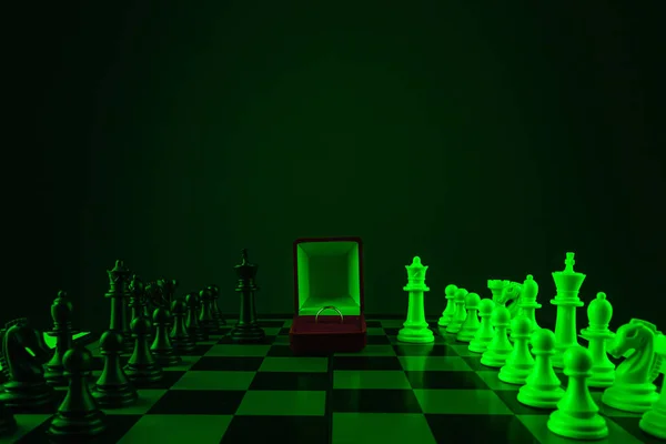 Chess pieces on a chessboard and a box with a golden ring, game. The concept of confrontation, career, competition, startup, truce, marriage, partnership