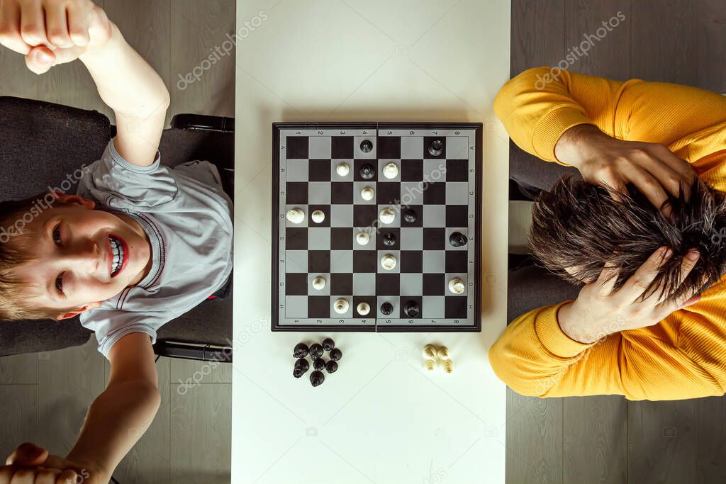 The boy rejoices in chess victory over his father. They play chess, family relationships, family. flat lay