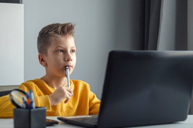 Sarı ceketli bir çocuk, evde bir masada oturuyor, bir dizüstü bilgisayara bakıyor, internetten öğreniyor, evde internet üzerinden öğreniyor. Teknoloji, okul, bilgi. Boşluğu kopyala