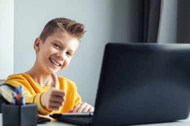 Sarı ceketli bir çocuk, evde bir masada oturuyor, bir dizüstü bilgisayara bakıyor, internetten öğreniyor, evde internet üzerinden öğreniyor. Teknoloji, okul, bilgi. Boşluğu kopyala