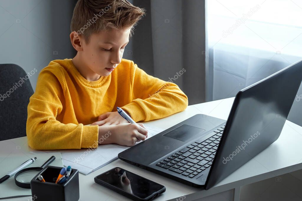 Distance learning, a boy learns math while looking at a laptop beech during an online lesson. The concept of online education, home education, technology, quarantine, self-isolation