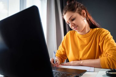 Evde dizüstü bilgisayar kullanan güzel bir kız, online eğitim konsepti, dizüstü bilgisayarın arkasında fen eğitimi alıyor. Webinar izlemek, sosyal ağlarda arkadaş aramak. Modern teknolojiler