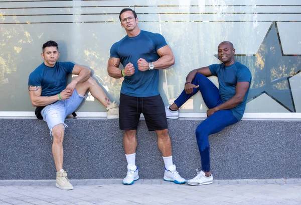 Tres hombres de diferentes grupos étnicos muy musculosos delante de un gimnasio —  Fotos de Stock