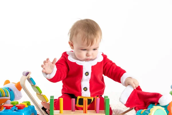 Bebê vestido de Papai Noel brincando com brinquedos de madeira e plástico e tocando seu chapéu Imagem De Stock