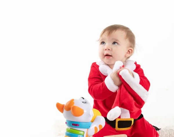 Bebê disfarçado de Papai Noel sentado no chão enquanto uma mão adulta agarra seu chapéu de suas mãos — Fotografia de Stock