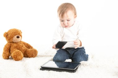 Bebek tabletle, cep telefonuyla ve oyuncak ayıyla oynuyor.