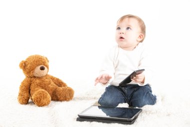 Elinde cep telefonu, tableti ve oyuncak ayısıyla bir bebek.