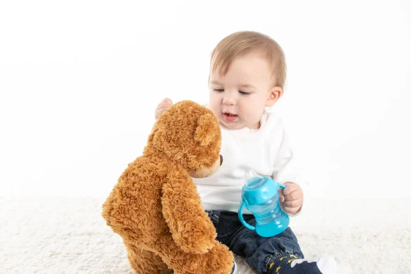 Baby met een veldfles met handgrepen en een teddybeer. — Stockfoto