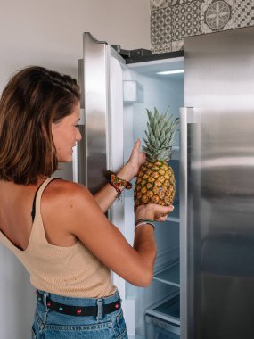 Sarışın ve genç bir kadın mutfağının buzdolabını açıyor..