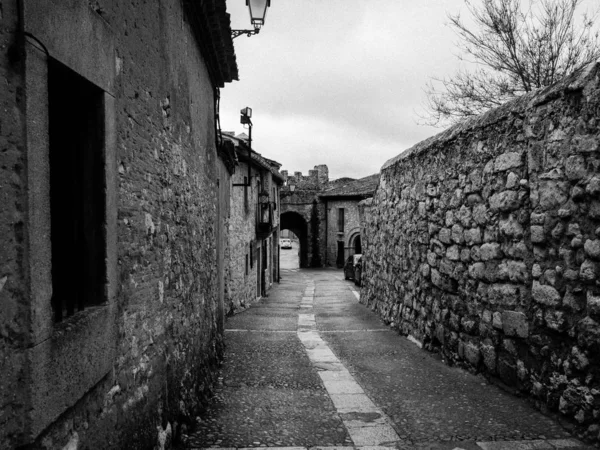 Foto in bianco e nero di una stradina circondata da muri in pietra con un tunnel in pietra sullo sfondo — Foto Stock