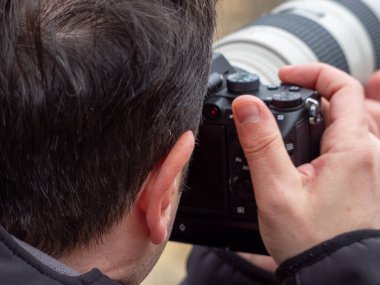 View from behind of a man taking a photograph with a reflex camera and a zoom lens