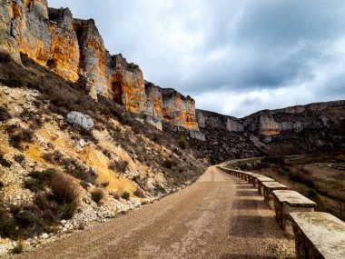Sandy path surrounded by rocky mountains and a small stone wall