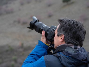 Adamın biri refleks kamerası ve yakınlaştırma lensiyle fotoğraf çekiyor.