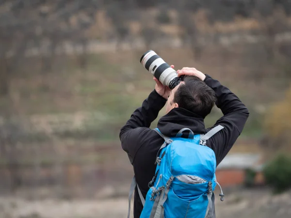 Homme avec un sac bleu prenant une photo avec un appareil photo réflexe et un zoom au milieu de la montagne — Photo