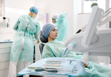 Tek kullanımlık Hap ve bornozlu genç bir kadın. Sandalyede oturup dişçi ve asistanı bekliyor. Klinikte iyileşme prosedürüne hazırlanıyor.