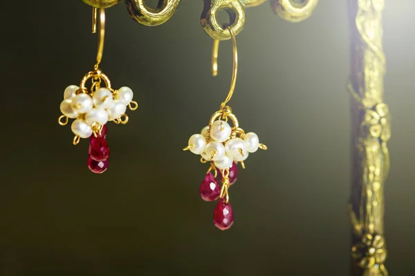 Boucles d'oreilles dorées avec rubis rouges avec perles blanches sur fond noir . — Photo