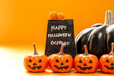 Turuncu arka planda izole edilmiş bir sürü turuncu balkabağı ve büyük siyah bir balkabağı ve siyah billboard. Cadılar bayramınız kutlu olsun.