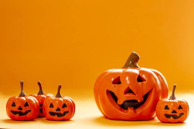 Birçok gülümseyen portakalın kabakları ve turuncu arka planda büyük bir balkabağı ve kopyalama alanı.