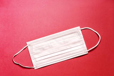 Tıbbi maske, kırmızı arka planda tıbbi koruyucu maske. Tek kullanımlık yüz maskesi ağız ve burnu kapatır. Sağlık ve Tıp Konsepti.