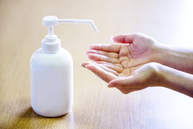 Bir kadın ellerine plastik sprey şişesinden antiseptik sıkar. Mavi arka planda yakın plan bir şişe ile eller. Salgın sırasında hijyenik tedavi.