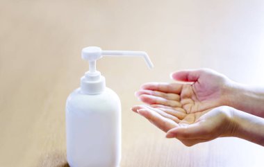 Bir kadın ellerine plastik sprey şişesinden antiseptik sıkar. Mavi arka planda yakın plan bir şişe ile eller. Salgın sırasında hijyenik tedavi.